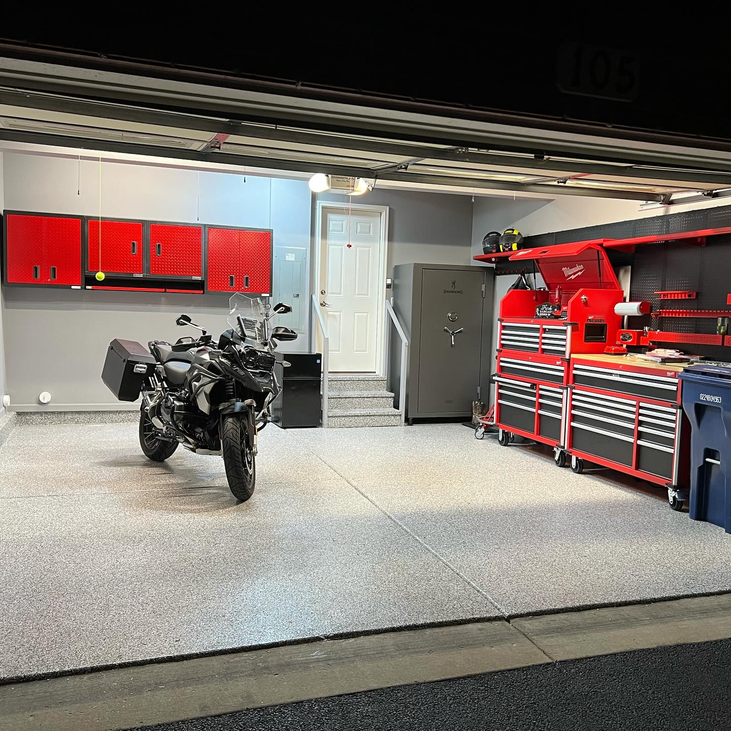 A neatly organized garage contains a parked motorcycle, red tool cabinets, and a sturdy safe beside a door leading indoors.
