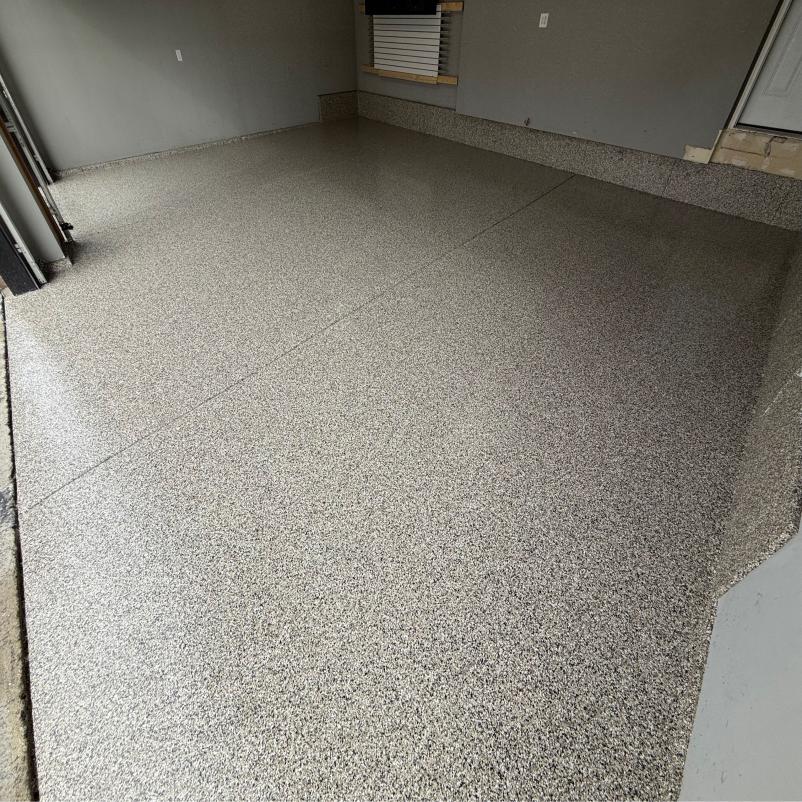 A garage features freshly coated, glossy epoxy flooring, gray walls, a small window with blinds, and a step leading to an interior door.