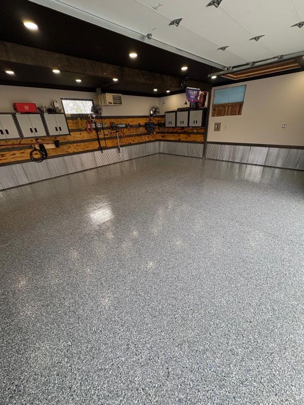 A clean, empty garage with polished terrazzo flooring, ceiling lights, metal cabinets, and wooden accents on the walls. Equipment neatly organized.