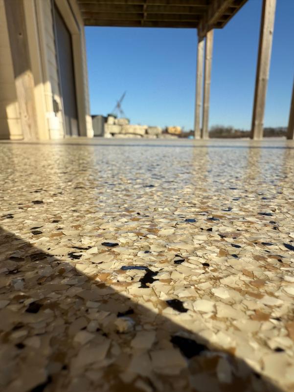 A terrazzo floor with sunlight, wooden beams, and a distant view of construction cranes and buildings under a clear blue sky.