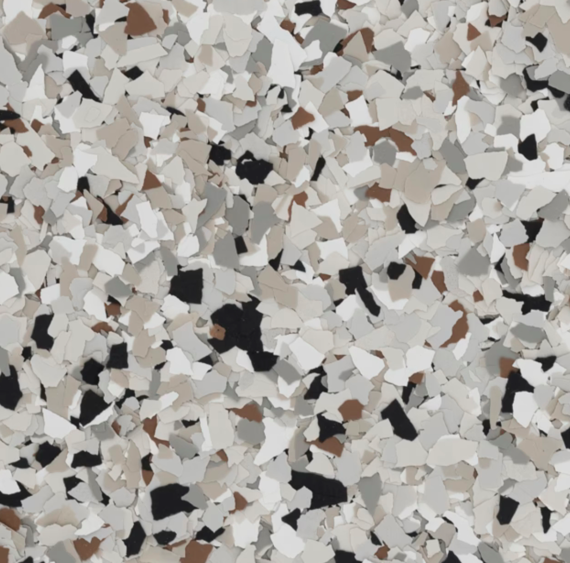 A close-up image of a surface with scattered multicolored decorative flakes in white, brown, and black tones, resembling a terrazzo pattern.