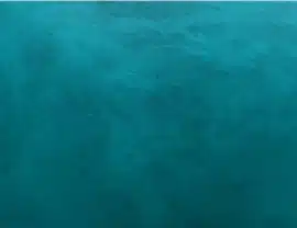 Aerial view of a vast, calm ocean with varying shades of blue and subtle surface ripples, showing no visible structures or people.