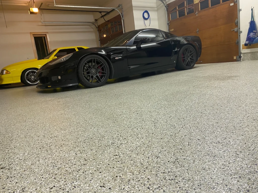 Two sports cars, one black and one yellow, are parked inside a spacious garage with a polished floor and wooden doors.
